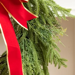 Close-up detail of artificial green pine needles with a large red and gold ribbon bow.