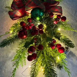 Festive Christmas teardrop swag detail with warm LED lights and red berries decoration.