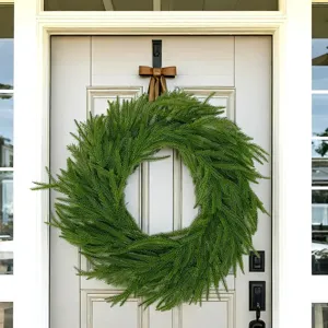 Detailed view of a lush green Norfolk pine wreath hanging on a front door for Christmas.