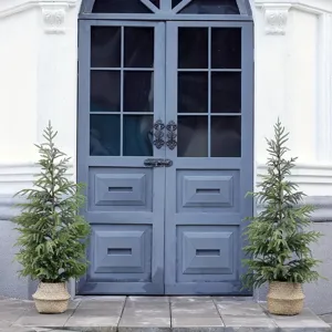 Paar künstliche Kiefern in Weidenkörben vor einem blauen Hauseingang zur Dekoration.