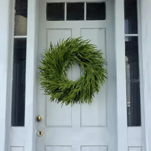 Artificial fern wreath hanging on a light blue front door for home decoration