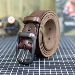 Detail shot of vintage brown genuine leather belt with dark metal pin buckle, workshop style.