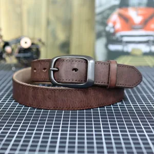 Detailed shot of retro brown leather men's belt with dark metal pin buckle on grid mat.