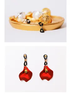 Detailed view of red petal drop earrings featuring small gold bells and black elastic band.