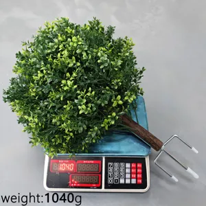 Close-up of a lifelike artificial boxwood bush being weighed on a scale at 1040g
