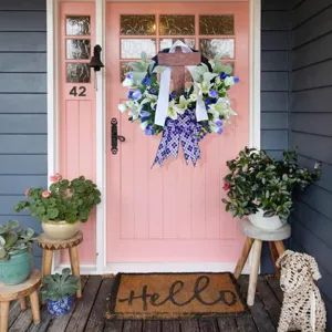 Easter wreath with a wooden cross and lily flowers hanging on a pink front door porch