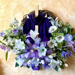 Detailed close-up of an Easter cross wreath featuring a purple drape and white lilies