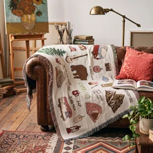 Cozy bohemian woven camping throw blanket with outdoor adventure patterns on a leather sofa