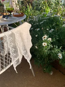 Detail shot of beige French lace floral triangular scarf draped on chair in garden background