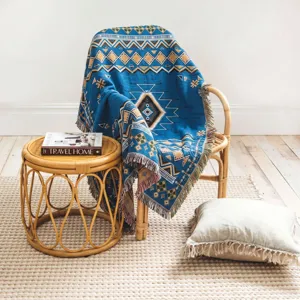 Manta tejida bohemia azul con flecos sobre una silla de mimbre en un ambiente acogedor.