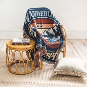 Cozy woven Bohemian camping blanket with wanderlust mountain design on a rattan chair