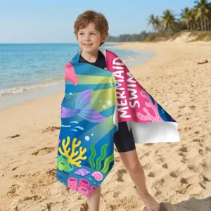 Junge mit buntem Meerjungfrau-Mikrofaser-Strandtuch an einem sonnigen Sandstrand