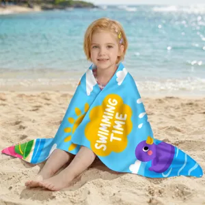 Mädchen am Strand in einem blauen Mikrofaser-Strandtuch mit 'Swimming Time' Aufdruck eingehüllt