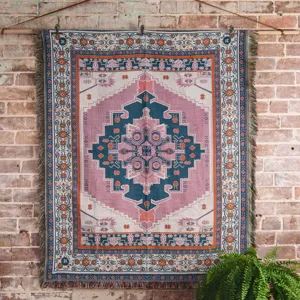 Manta tejida bohemia con patrones geométricos rosa y verde azulado sobre pared ladrillo.