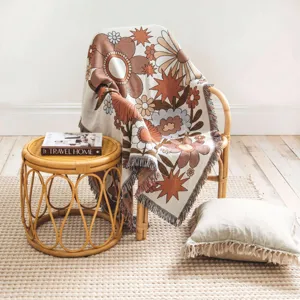 Retro bohemian floral woven throw blanket draped over a rattan chair in a cozy minimalist room