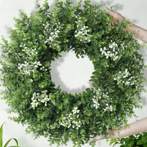 Large lush green eucalyptus wreath with white berry accents held against a light wall
