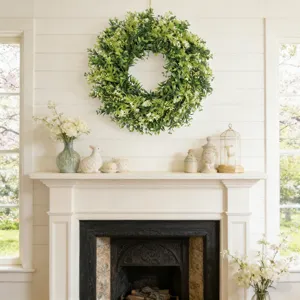 Luxe kunstmatige buxuskrans met witte wilde bloemen boven een witte schouw hangend