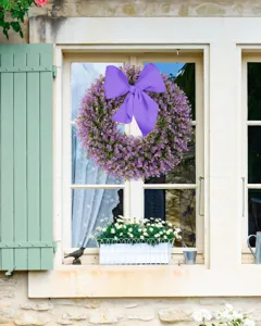 Purple artificial eucalyptus wreath with a large bow hanging on a cream cottage window