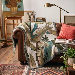 Detail of tropical leaf woven throw blanket draped over a vintage leather sofa