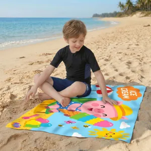 Kind sitzt auf einem farbenfrohen Mikrofaser-Strandtuch mit Cartoon-Schwein am Strand
