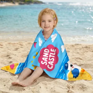 Mädchen in blauem Mikrofaser-Strandtuch mit buntem Sandburg-Druck am Strand gewickelt