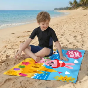 Junge sitzt auf einem bunten Mikrofaser-Strandtuch mit Sandburg-Motiv am sonnigen Strand