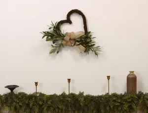 Heart-shaped olive branch wreath with burlap bow hanging on a white wall as home decor