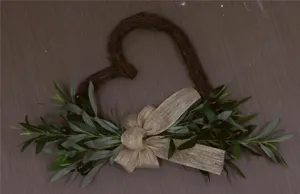 Macro detail of a rustic heart-shaped vine wreath featuring artificial olive branches and bow