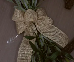 Detailed close-up showing a rustic burlap bow tied on artificial green olive leaves wreath