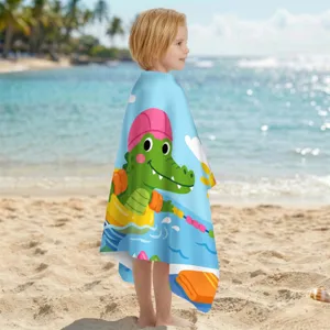 Kind in einem süßen Mikrofaser-Strandtuch mit Krokodil-Motiv an einem sonnigen Sandstrand