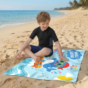 Kind sitzt auf einem bunten Mikrofaser-Strandtuch mit Wal-Motiv im weichen Sand