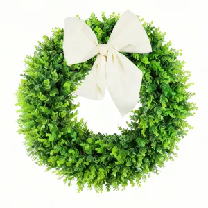 Weelderige groene buxuskrans met grote roomwitte strik voor decoratie aan de voordeur