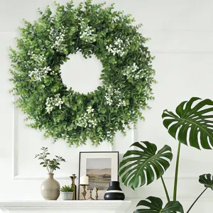 Lush artificial boxwood wreath with white berries displayed on a white interior wall.