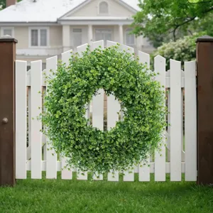 Lush green artificial boxwood leaf wreath hanging on a white wooden garden fence