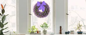 Elegant purple artificial eucalyptus wreath with bow hanging on a bright white window frame