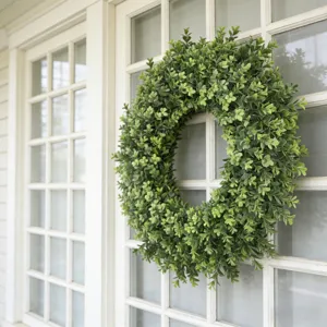 Macro view of a lush green artificial boxwood wreath hanging on a white window frame.