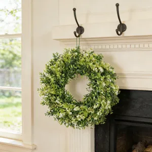 Kunstmatige buxus wildbloemen krans hangend aan een witte schoorsteenmantel decor