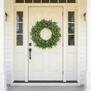 Realistic artificial boxwood wreath displayed hanging on a classic white front door scene.
