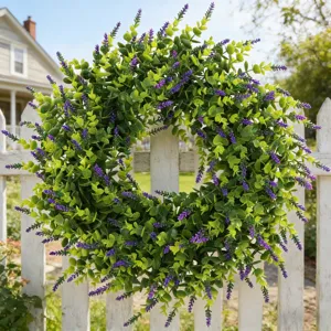 A detailed view of a lush artificial lavender and boxwood wreath hanging on a white fence.
