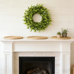 Kunstmatige eucalyptuskrans aan een witte muur boven een moderne binnenhaard