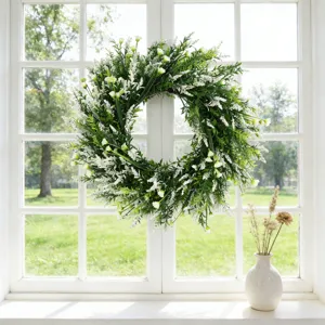 Lush green artificial wreath with delicate white flowers hanging on a sunlit window frame