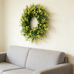 Artificial yellow flower wreath hanging on a cream wall above a modern gray sofa