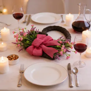 Dettaglio di una ghirlanda a forma di cuore con fiori rosa su una tavola apparecchiata.