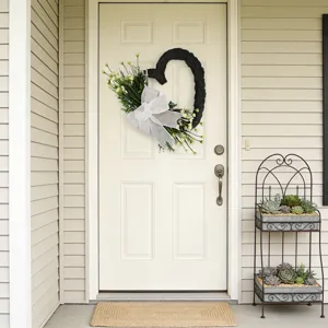 Ghirlanda floreale nera a forma di cuore con fiocco bianco su una porta d'ingresso