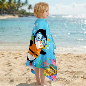 Kind am Strand eingewickelt in ein schnell trocknendes Strandtuch mit Pinguin-Motiv