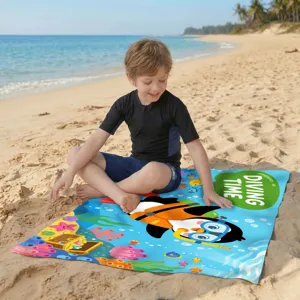 Kleinkind sitzt auf einem bunten Mikrofaser-Strandtuch mit Cartoon-Pinguin-Motiv
