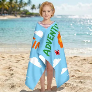 Kleines Mädchen in einem blauen Mikrofaser-Strandtuch mit Adventure-Aufdruck am Strand.