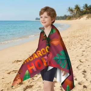 Kleiner Junge am sonnigen Strand in ein rotes Mikrofaser-Strandtuch mit Kängurumuster gehüllt