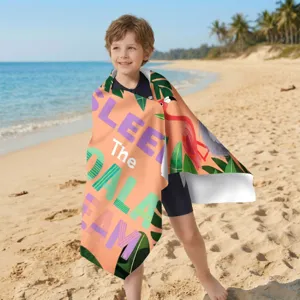 Kind eingehüllt in ein schnelltrocknendes Mikrofaser-Strandtuch mit Flamingo-Print am Strand
