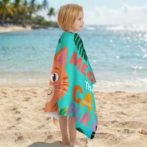 Kind in einem Mikrofaser-Strandtuch mit Katzenmotiv am sonnigen tropischen Strand